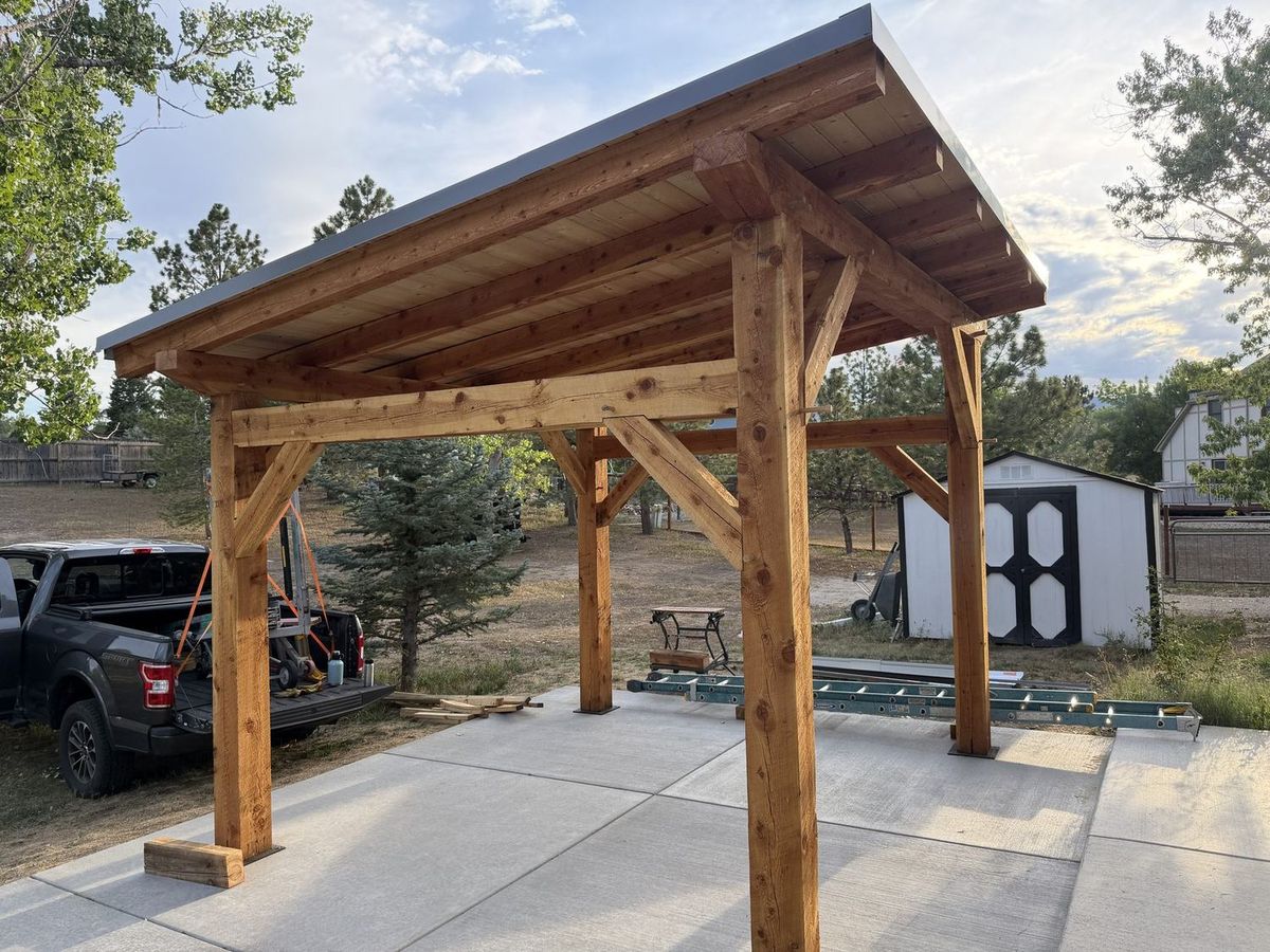 Timber frame pavilion nearing completion in an Arvada backyard, with a truck and tools staged nearby