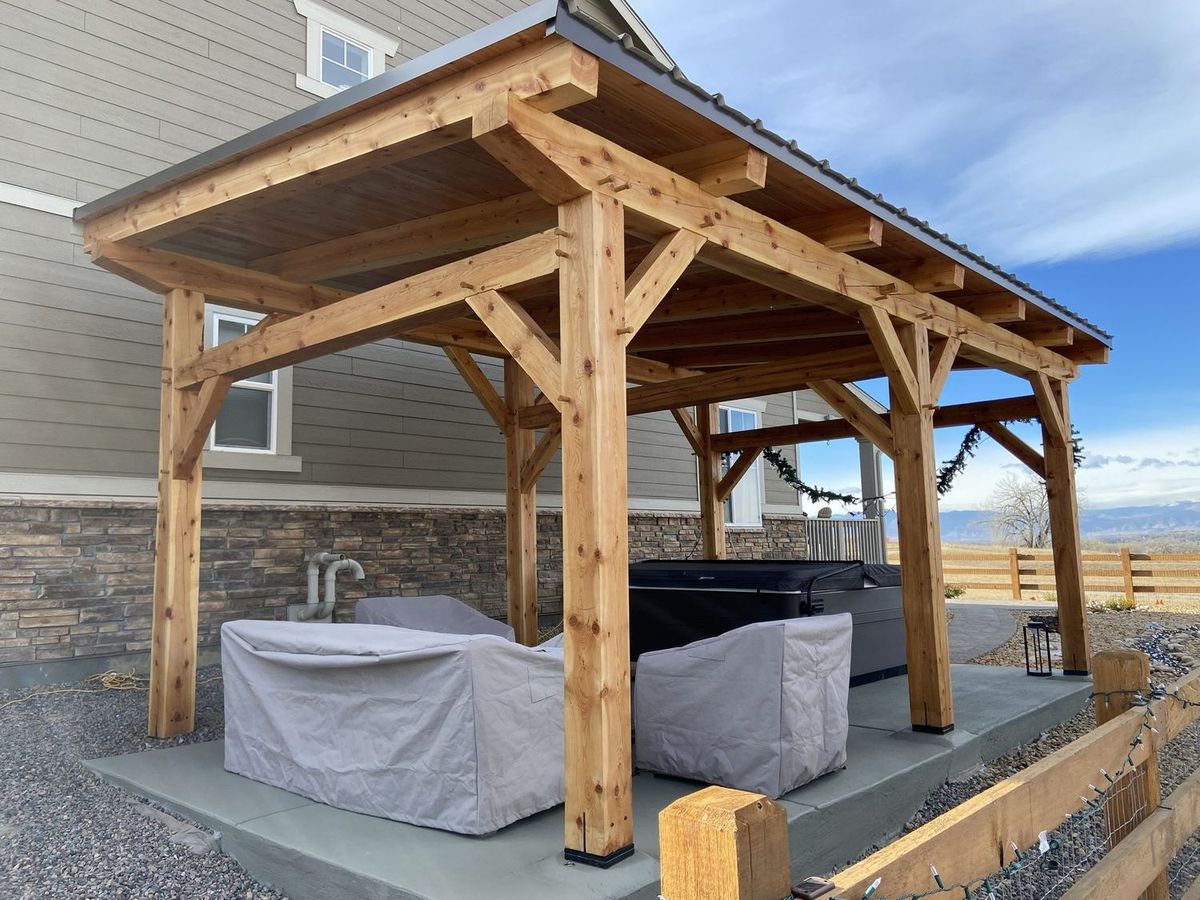 Timber frame pavilion with a hot tub under the roof and covered patio furniture beside it