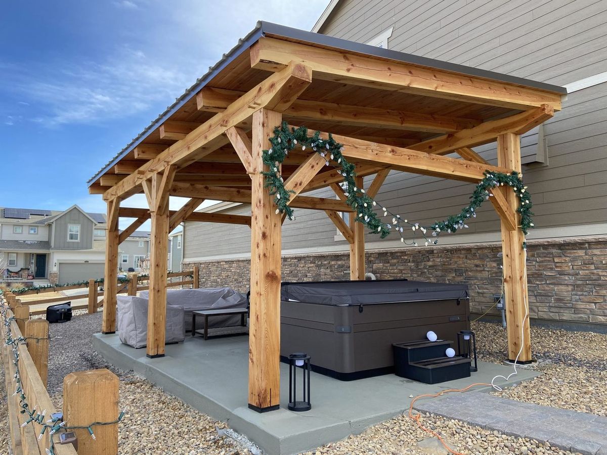 Finished timber frame pavilion with a green garland along the beams and a hot tub beneath the roof