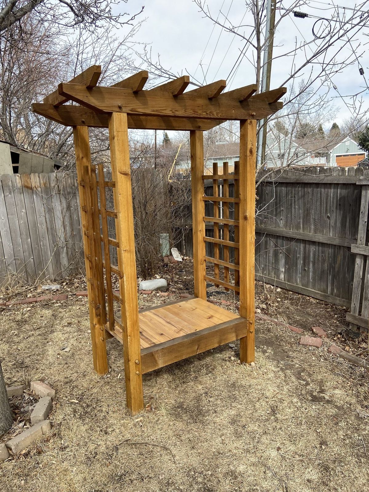 Cedar arbor with lattice sides and a plank bench, seen from a second angle