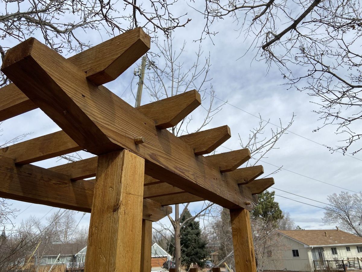 Rafter tails and a cross beam on a small cedar arbor, seen from below against a cloudy sky