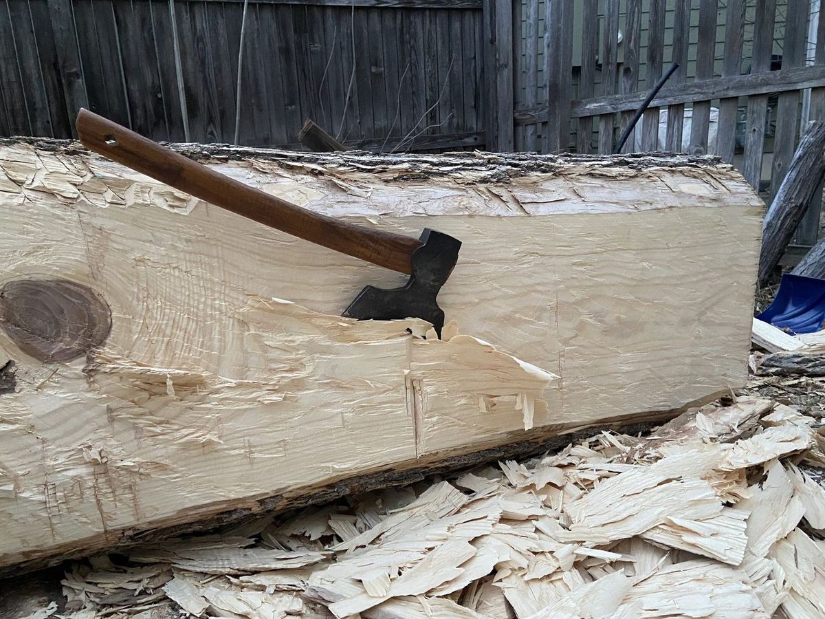 A hewn beam face being flattened by hand, with tool marks visible along the wood