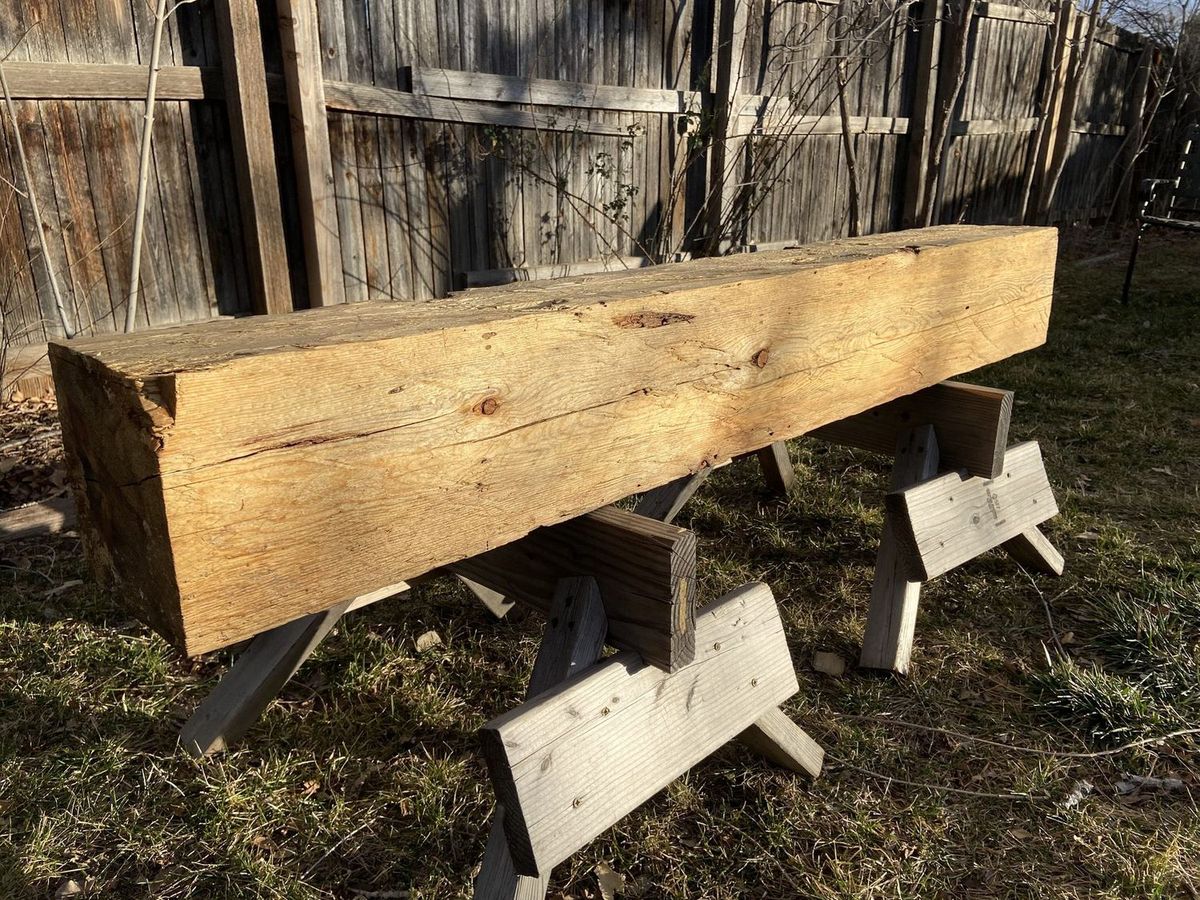 A large hand-hewn beam on sawhorses in low sun, ready to become a mantel